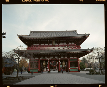 Senso-ji Temple in Tokyo, Japan, features traditional Japanese architecture with red and gray tones, a blue sky, and trees.