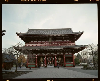 Senso-ji Temple in Tokyo, Japan, features traditional Japanese architecture with red and gray tones, a blue sky, and trees.