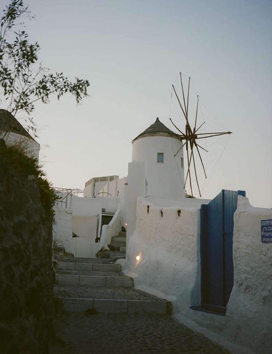 Stone steps lead up to a white windmill in Santorini, Greece, under a soft, early morning sky. Architectural shot. Peaceful travel destination.