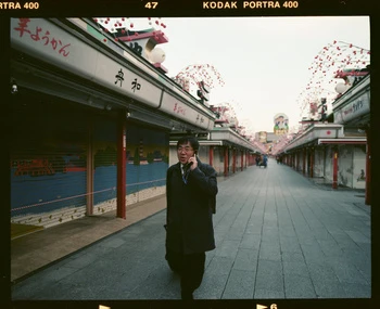 Man in coat walking through covered market street in Japan, talking on mobile phone, with shops and stalls closed.