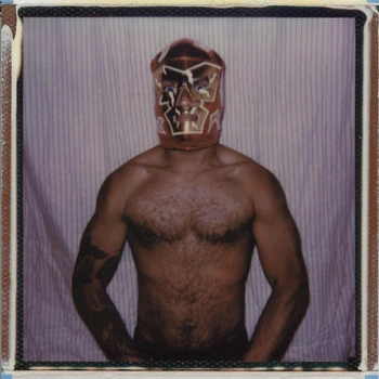 Portrait of a shirtless male wrestler wearing a red patterned mask against a striped backdrop. Arms are bent at the elbows.