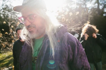 Group of people in outdoor setting, backlit by the sun. One man in foreground wears colorful glasses and jacket.