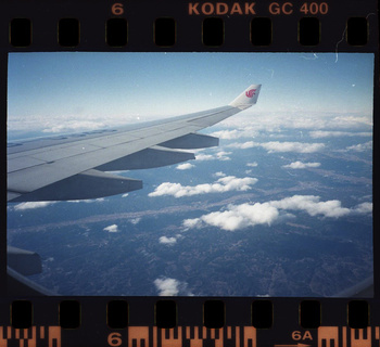 Airplane wing with China Eastern Airlines logo over a scenic view of a landscape with clouds and landforms on a sunny day.