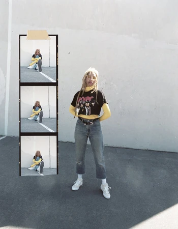 Young adult with dreadlocks wearing a band t-shirt, jeans, and sneakers stands against a white wall, next to a contact sheet of images.
