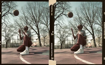 Young adult playing basketball on an outdoor court. Urban setting with overcast lighting and film aesthetic for youthful fashion editorial.