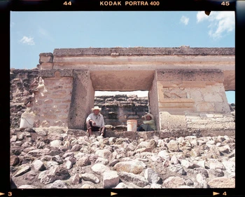 Two men sit among weathered stone ruins of an old structure in a desert landscape beneath a sunny blue sky, photographed on Kodak Portra 400 film.