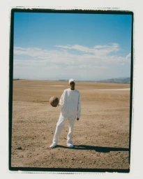Person wearing all white clothing holding a basketball in a barren desert landscape under a clear blue sky