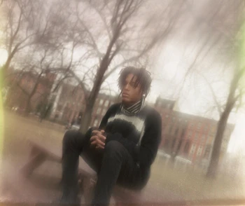 Young man with dreadlocks seated outdoors wearing dark sweater and striped scarf photographed by Levi Walton