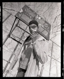 Black man holding a magnifying glass to his eye standing on a basketball court photographed in monochrome film by Levi Walton