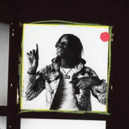 Monochrome portrait of a man wearing a patterned hoodie pointing upward, presented inside film borders.