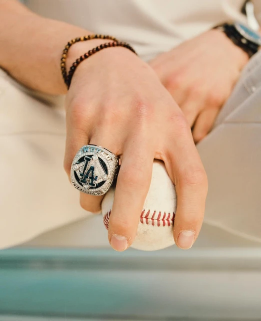 Close-up of a hand holding a baseball, adorned with a large Dodgers World Series ring, capturing a moment of sports glory.