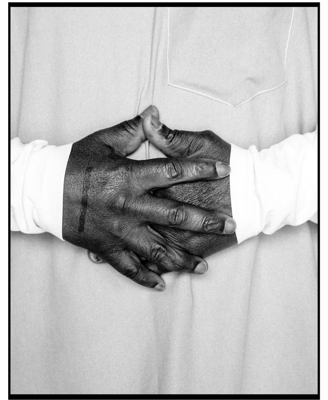 Close-up black and white shot of an African American person's interlaced hands resting on light grey fabric with a white pocket detail.