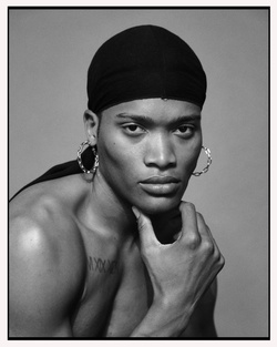 Striking black and white portrait of a shirtless person with a durag, hoop earrings, and hand on chin, set against a neutral gray background.