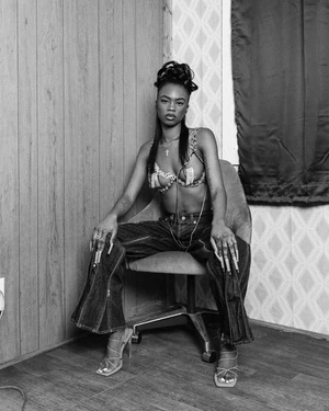 Black woman seated in an office chair wearing a decorative bralette and wide-leg denim jeans in Los Angeles by Maiwenn Raoult.