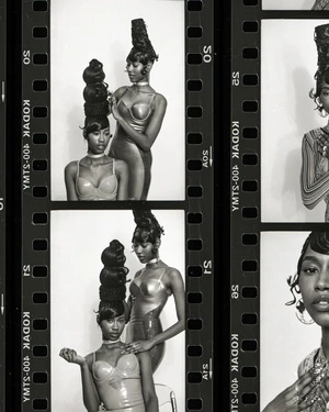 Two Black women with sculpted updos pose in studio with vintage film strip border. Beauty shot with high-fashion hairstyle and neutral makeup.