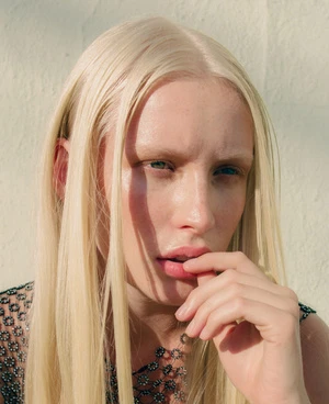 Portrait of a blonde woman with long hair and light eyebrows posing against a textured wall in Los Angeles.
