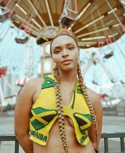 Woman posing in yellow Jamaica top with amusement park in background. Portrait of a tan-skinned woman in bright outdoor setting.