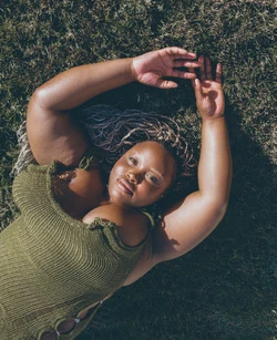 Overhead portrait of plus-size woman with silver-blonde hair lying on a lawn wearing a green knitted top, summer fashion.