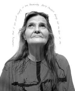 Portrait of an older woman looking upward wearing a graphic t-shirt against a plain white background with handwritten text above her head
