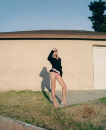 Blonde woman in black top shielding her eyes against a residential building exterior by photographer Maiwenn Raoult