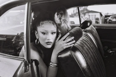 Black and white portrait of a woman seated in the back seat of a car looking toward the camera, photographed by Maiwenn Raoult.