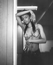 Black woman with long manicured nails posing in an interior doorway wearing a decorative embellished body chain and jeans.