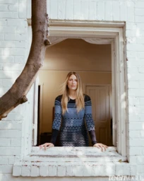 Woman in patterned long-sleeve dress leaning on a white brick window frame outdoors in Los Angeles