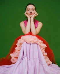Woman wearing multi-layered pink and lilac dress posing against solid green backdrop by photographer Maiwenn Raoult.