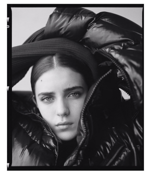 Portrait of a woman wearing a glossy black puffer jacket and dark hat captured by Matthew Priestley