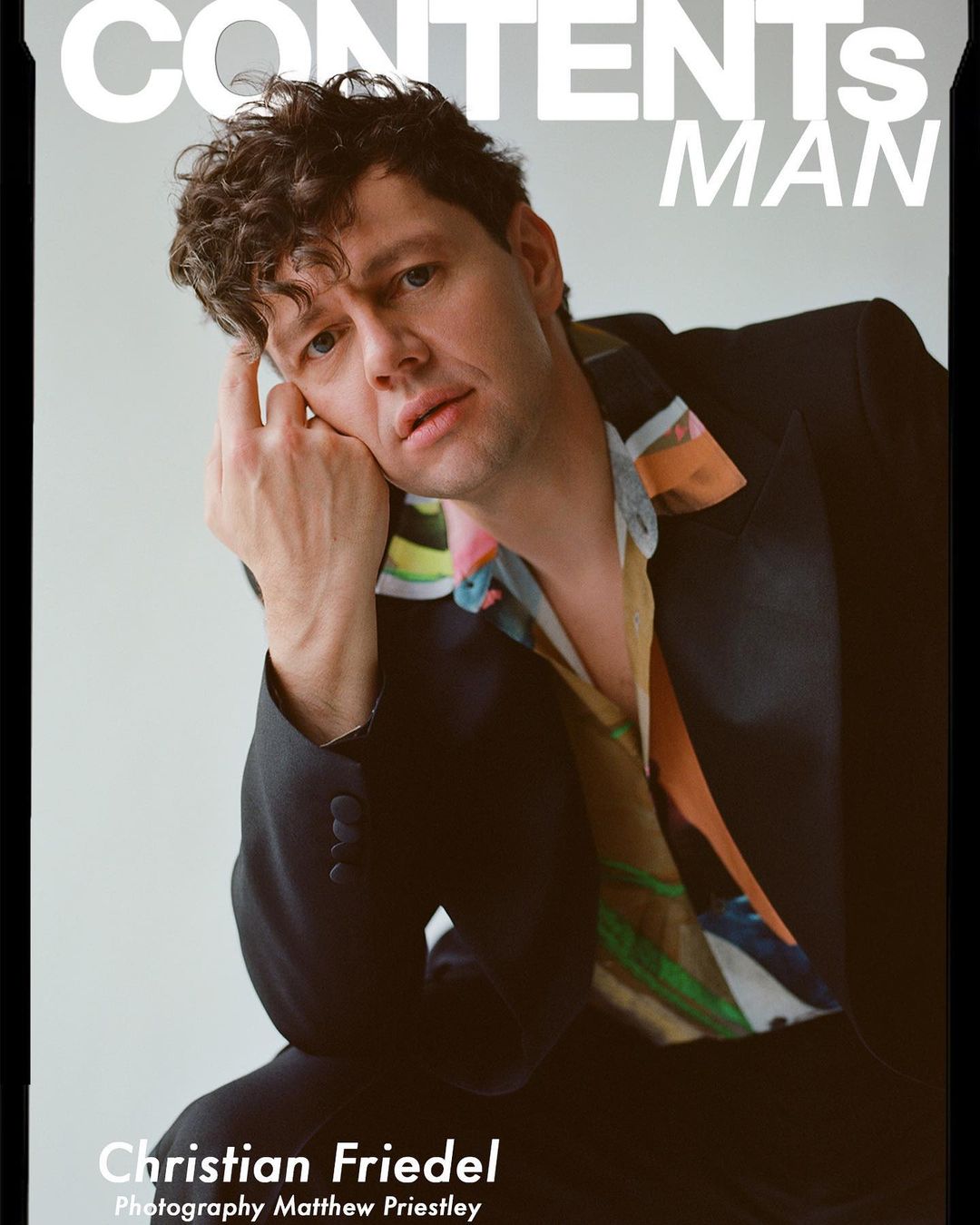 Portrait of Christian Friedel wearing a dark suit jacket and patterned shirt, photographed by Matthew Priestley.