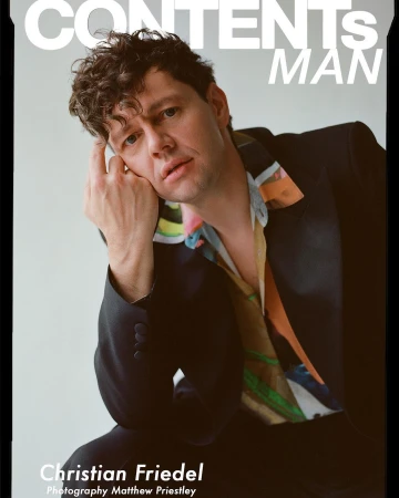 Portrait of Christian Friedel wearing a dark suit jacket and patterned shirt, photographed by Matthew Priestley.