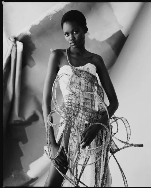 Monochrome portrait of a Black woman in a white dress adorned with film strips against an abstract painted backdrop in a photo studio.