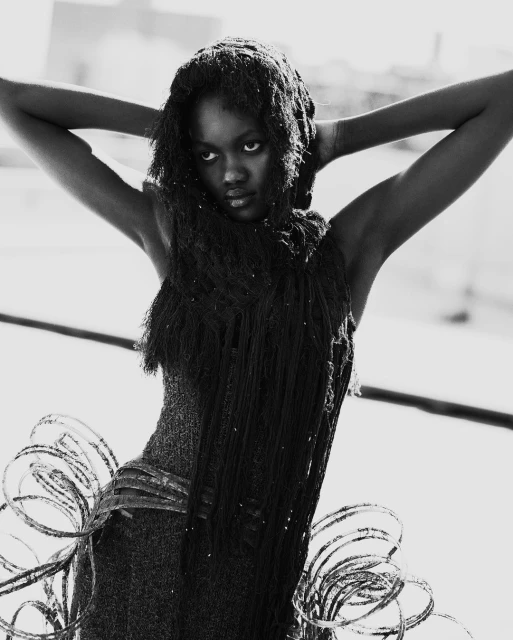 Black and white portrait of a Black woman with arms raised and hair draped around her head and shoulders in a fashionable garment.