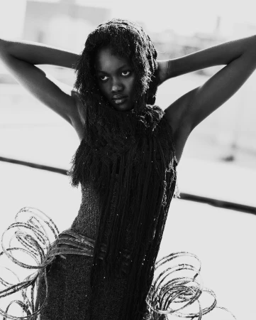 Black and white portrait of a Black woman with arms raised and hair draped around her head and shoulders in a fashionable garment.