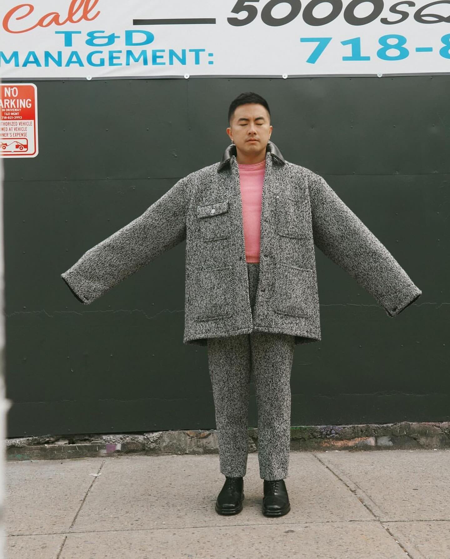 Man wearing a textured grey tweed jacket and matching trousers with arms outstretched on a sidewalk.
