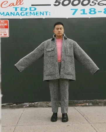 Man wearing a textured grey tweed jacket and matching trousers with arms outstretched on a sidewalk.