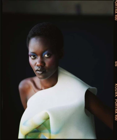 Portrait of a black woman wearing a sculpted white top and colorful blue eyeshadow against a dark background