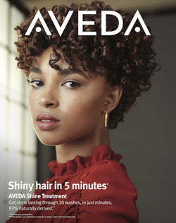Close-up of a young adult woman with curly brown hair, wearing a reddish-brown blouse and gold earrings, posing in front of window light.