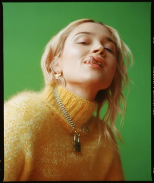 Blonde woman in yellow sweater against green background. Portrait of a smiling young adult female model with natural makeup.