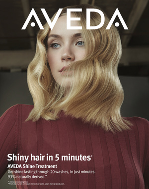 Aveda ad featuring a woman with blonde wavy hair and fair skin looking off-camera, wearing a dark red sweater, against a neutral backdrop.