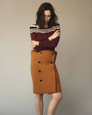 A woman wearing a skirt with button detailing and a striped sweater poses against a neutral background in a studio shot.