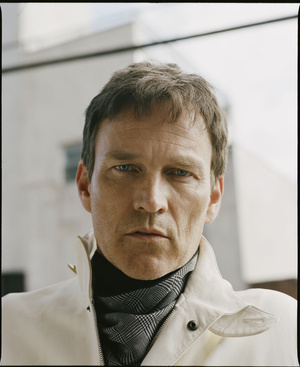 Close-up portrait of a man with short brown hair wearing a white jacket and patterned scarf by photographer Matthew Priestley.