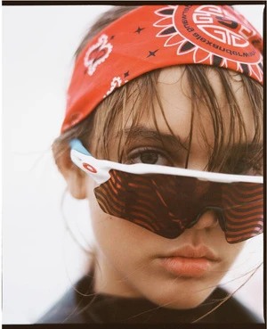 Close-up studio portrait of a young woman with red bandana, sunglasses, and glossy skin. Fashion and beauty editorial shot.