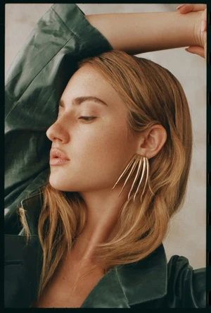 Close-up portrait of a woman wearing gold claw earrings and a dark green jacket by Matthew Priestley