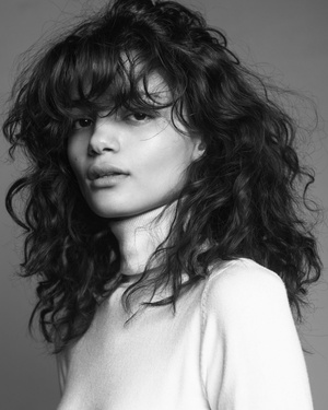Portrait of a woman with curly hair and bangs wearing a light top in monochrome