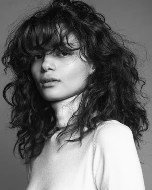 Portrait of a woman with curly hair and bangs wearing a light top in monochrome
