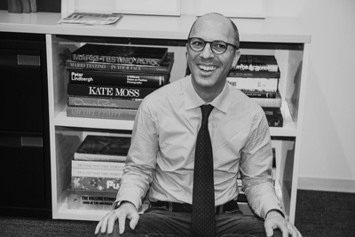 Portrait of a smiling man wearing glasses, a collared shirt, and a tie seated in an office by Matthew Priestley