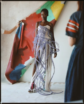 Black female model wearing an avant-garde structured dress with looping purple ribbon embellishments in a studio.