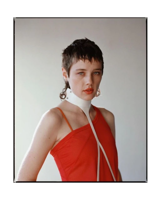 Portrait of a woman with short hair, wearing a red top and white collar, against a neutral backdrop, showcasing fashion and beauty.