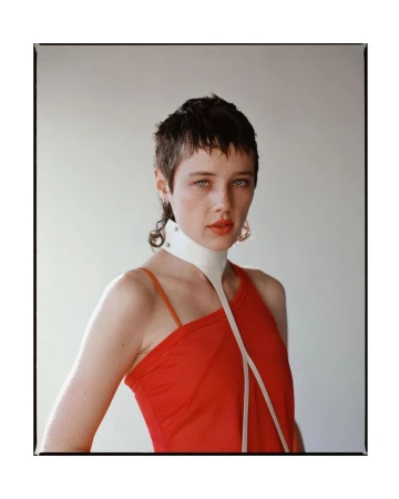 Portrait of a woman with short hair, wearing a red top and white collar, against a neutral backdrop, showcasing fashion and beauty.